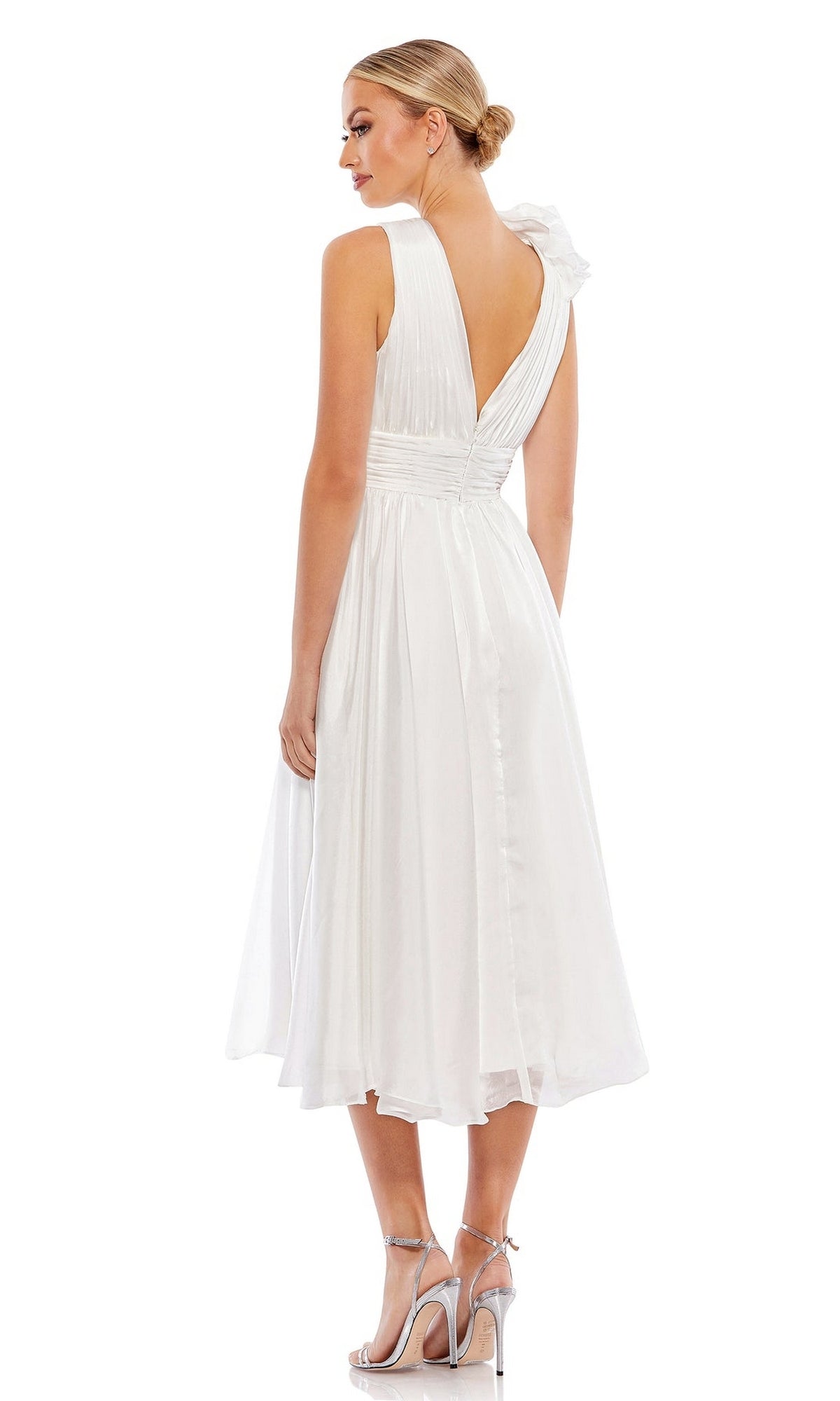 A woman wears the Short Wedding Guest Dress 70165 by Mac Duggal—a white, sleeveless, knee-length dress with a ruched ruffled bodice and asymmetrical shoulder—paired with silver heels against a white background.